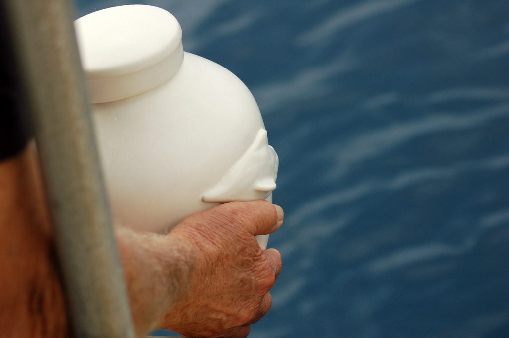 A man holding a white urn with ashes moments before pouring those ashes in a body of water
