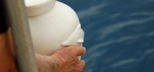 A man holding a white urn with ashes moments before pouring those ashes in a body of water