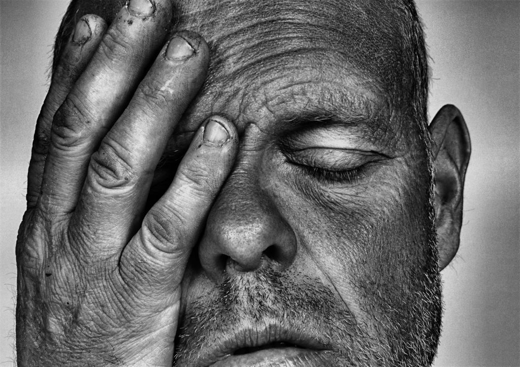 An older man with eyes closed and covering part of his face with his hand can show the predatory energy known as curse