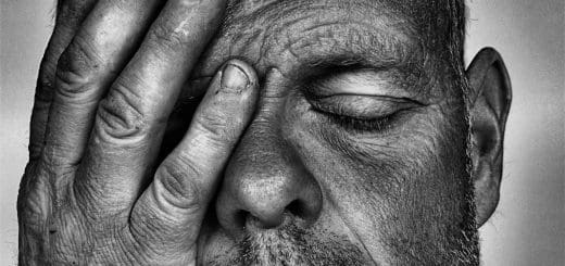 An older man with eyes closed and covering part of his face with his hand can show the predatory energy known as curse