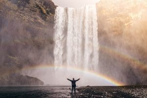 A person appreciating a rainbow cast by a waterfall. Wellness and healing can be achieved in a session